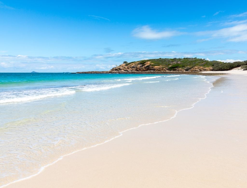 A pristine white-sand beach with clear turquoise water gently lapping the shore.